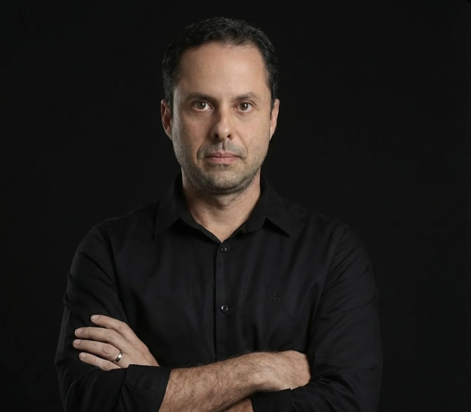 Retrato de Fernando Saback, de braços cruzados, com camisa preta sobre fundo preto